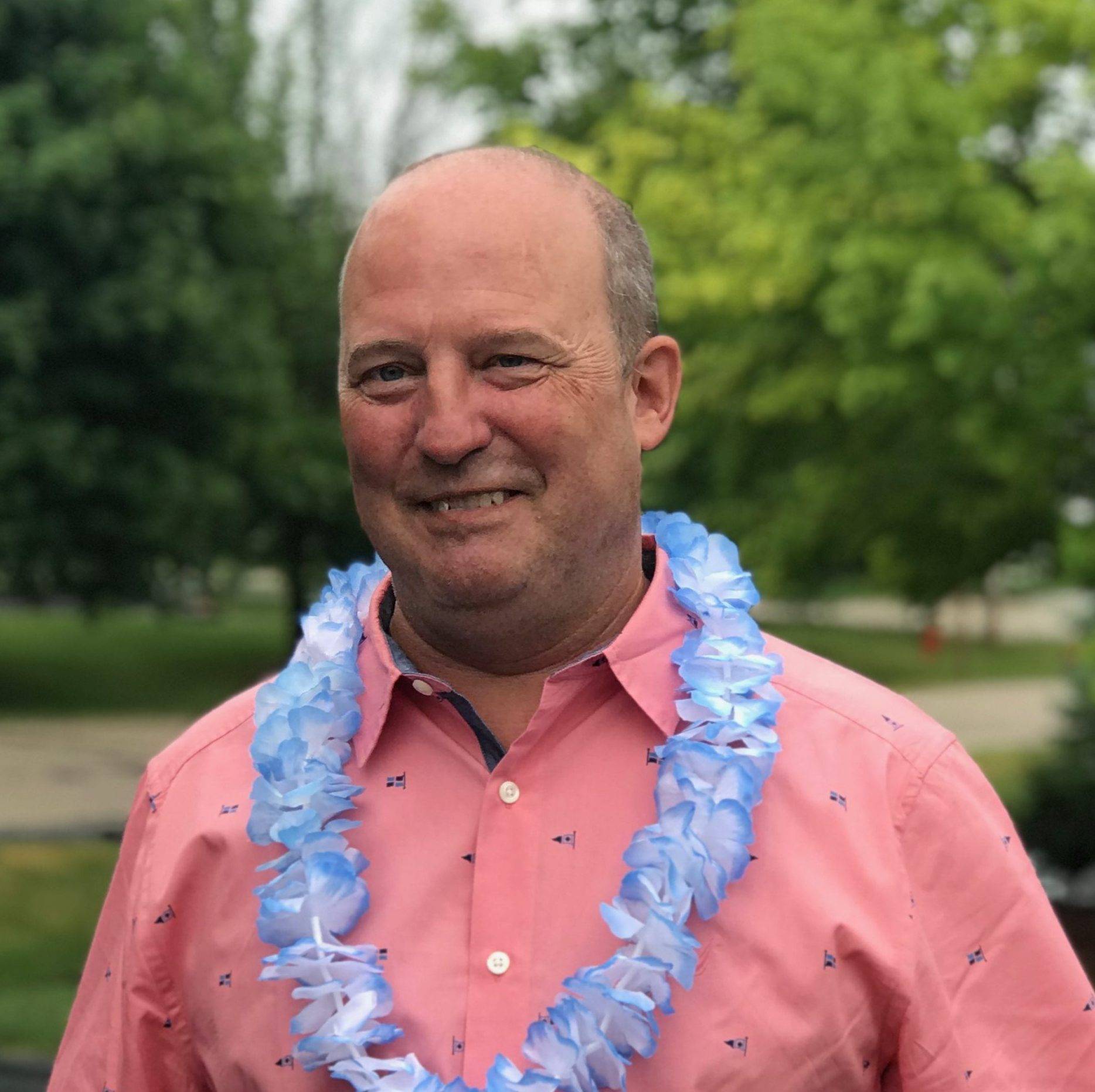 Tom Trott in a pink collared shirt and a blue Leis.